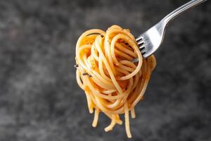 A fork holding a serving of spaghetti against a dark background. photo