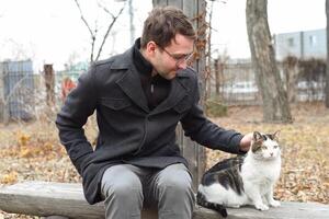 Young man sitting on bench and petting a cat photo