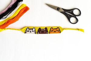 Woven DIY friendship bracelet with Cats pattern handmade of embroidery floss on white background. photo