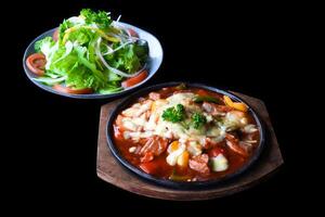 Stewed beef with cheese and vegetables on wooden plate isolated on black background side view photo