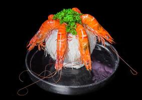 Five orange shrimps inside of coconut with sauce isolated on black background top view photo