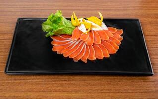 slicing appetizer of red fish slices on a black plate on a wooden table top view photo
