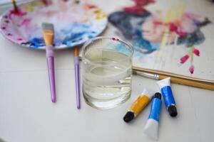paint brushes and water on a table with and palette for art photo