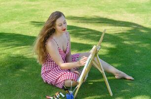 Young artist woman with paint brushes and easel close to sea and palms in summer photo