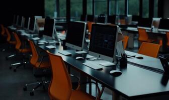 Modern computer lab with many desks and chairs. Rows of computers, dark tables, and bright orange chairs photo