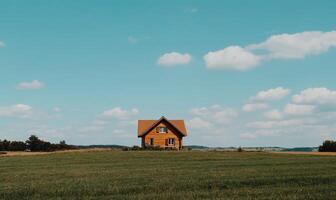 Quaint wooden house nestled in a vast green field under a clear blue sky photo