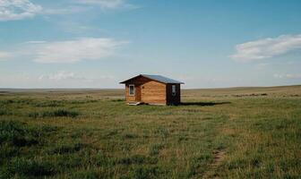 Rustic wooden cabin in a vast grassland landscape under a partly cloudy sky. Small, simple structure, nestled in the open field, evokes a sense of tranquility and solitude photo