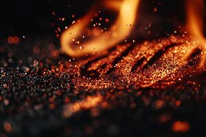 Fiery embers glow on dark surface. Tiny sparks fly photo