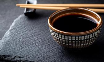 A cup of black soy sauce with chopsticks on a black slate photo