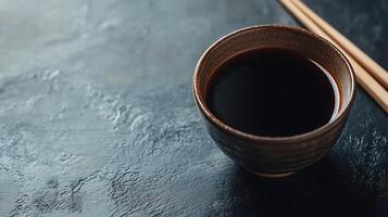 A cup of black soy sauce with chopsticks on a dark surface photo