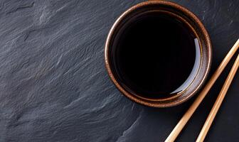 Dark Soy Sauce in Small Bowl with Chopsticks on Dark Stone photo