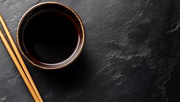 Dark soy sauce in bowl with chopsticks on a dark stone surface photo