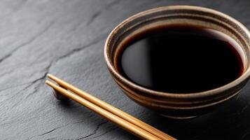A cup of black soy sauce with chopsticks on a black background photo