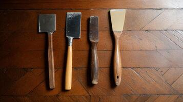 Four vintage painting tools on a wooden table. Different sizes and materials, likely used for applying or removing paint photo