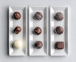 Delectable chocolate truffles arranged on three white rectangular plates. Assorted shapes, colors, and textures photo