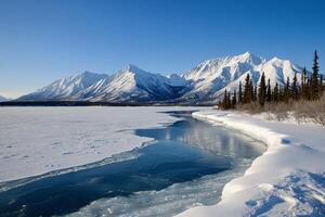 Frozen river meanders through snowy mountains under a clear blue sky photo