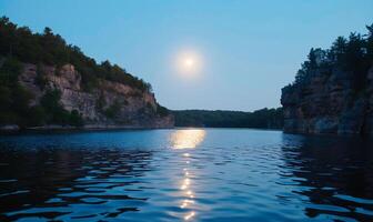 Serene lake at dusk with a full moon reflecting. Rocky cliffs frame the tranquil water photo