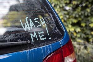 Dirty car window displays WASH ME amidst grime, with a hint of red taillight photo