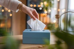 Hand retrieves tissue from blue box, with soft focus greenery in the background, evoking comfort photo