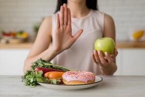 Woman gestures no with palm while holding a green apple, symbolizing healthy choices photo