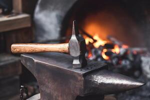 Weathered hammer rests on an anvil, surrounded by glowing forge embers photo