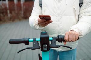 Handsome man using smartphone app. Guy approaches an electric scooter and using mobile phone app NFC contactless locker on bike bicycle in sharing parking lot. photo