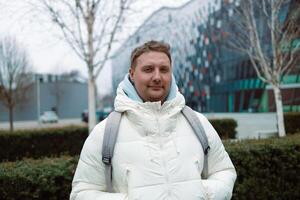 Portrait of Caucasian smiling bearded man with backpack, looking at camera aganist airport terminal building in the winter city. Lifestyle, city life concept photo
