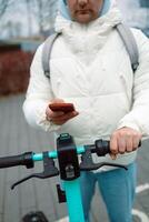 Handsome man using smartphone app. Guy approaches an electric scooter and using mobile phone app NFC contactless locker on bike bicycle in sharing parking lot. photo