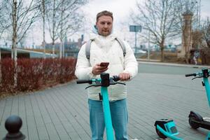 Handsome man using smartphone app. Guy approaches an electric scooter and using mobile phone app NFC contactless locker on bike bicycle in sharing parking lot. photo