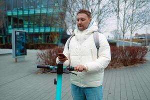 Handsome man using smartphone app. Guy approaches an electric scooter and using mobile phone app NFC contactless locker on bike bicycle in sharing parking lot. photo