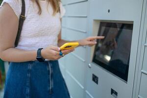 Woman using automated self service post terminal machine or locker to deposit the parcel for storage photo