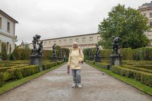 A female tourist walks around along a decorative alley decorated with many statues in a decorative park at Wallenstein Palace building in Prague in Czech Republic photo