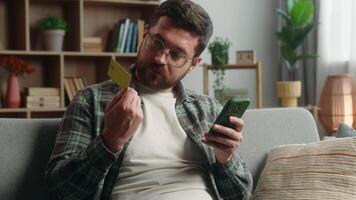 Caucasian man male guy at home worried upset with mobile phone and credit card problem shopping difficult failure buying online purchase trouble blocked account error looking at camera shrug shoulders video
