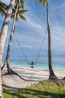 Woman on tropical beach swing, enjoying the ocean view and freedom under palm trees, a perfect island escape. photo