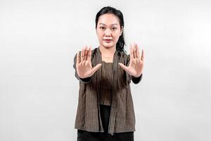 An Indonesian woman wearing traditional lurik attire smiles confidently while holding both hands up in a stop gesture, showcasing cultural pride and assertiveness against a neutral background. photo