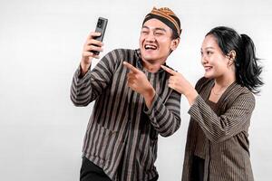 a Indonesian couple in traditional Javanese Lurik or Sorjan outfit taking a selfie together. Smiling, cheerful, and happy expression. Isolated on white background. photo