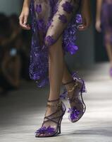 Model walking runway wearing purple lace dress and butterfly high heels photo