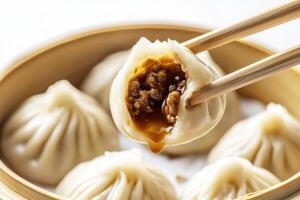 Chopsticks holding delicious xiaolongbao filled with soup and meat over steaming basket photo