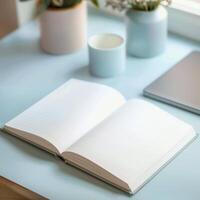 Open notebook on a blue desk with laptop and plant photo