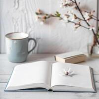 A book, a cup of coffee and a branch of cherry blossom on a white wooden table photo