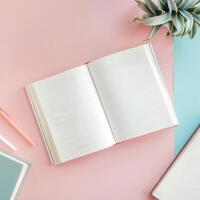 Open notebook, pen, pencils, and plant on pink and blue background photo