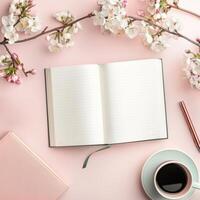 Open notebook, coffee cup, pen and flowers on pink background photo