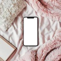 Blank smartphone on pink blanket with book and pillows photo