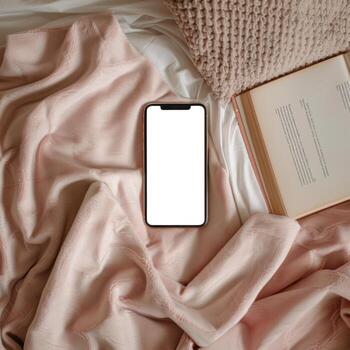 A smartphone is on a bed with a book and a pillow photo