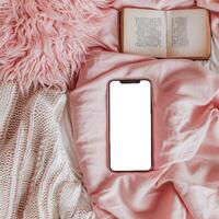 Blank iphone screen on pink blanket with book and fluffy pillow photo