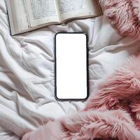 Blank iphone screen on a bed with a book and fluffy blanket photo