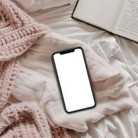 Blank smartphone on bed with book and knitted blanket photo
