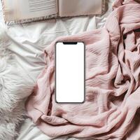 A white phone is sitting on a bed with a book photo