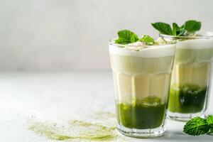 Glasses with matcha on white background with copy space, cup with green beverage, foam and tea leaves photo