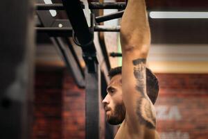 side view of a strong man doing pull ups in a gym. close-up photo